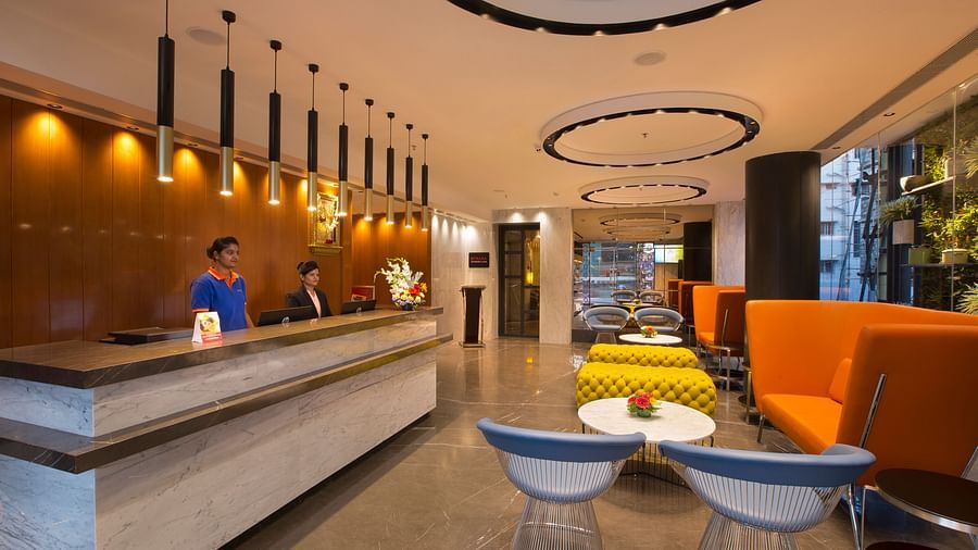 A modern hotel reception area with bright orange and yellow seating, a dark wooden front desk and pendant lights - Hotel Southend by TGI - Bommasandra, Bangalore