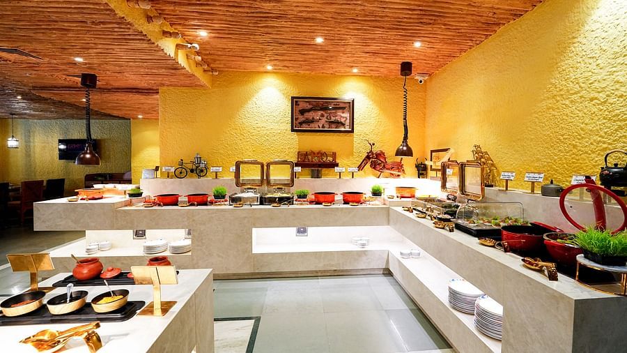 A comprehensive view of a buffet setup in a room with a rustic ceiling and yellow walls. - Tara, Comfort Hotel in Hyderabad - Ramoji Film City.