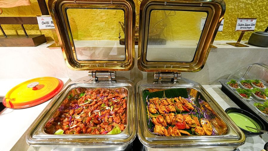 A buffet section with metal trays holding a selection of appetizing Indian dishes. - Tara, Comfort Hotel in Hyderabad - Ramoji Film City.