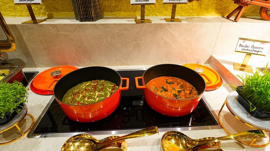 Colorful curries served in traditional pots alongside golden serving utensils. - Tara, Comfort Hotel in Hyderabad - Ramoji Film City.