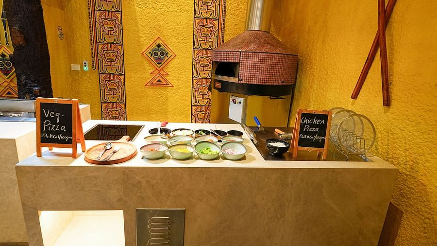 A cozy food station with a stone pizza oven against a yellow textured wall at Tara, Comfort Hotel in Hyderabad - Ramoji Film City.