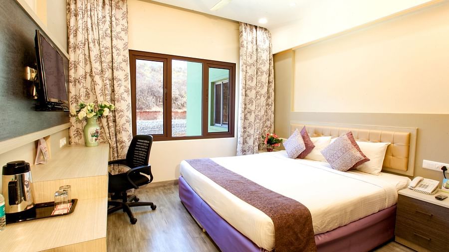 A modern hotel room with a plush king-sized bed and a view of the outdoors. - Tara, Comfort Hotel in Hyderabad - Ramoji Film City.