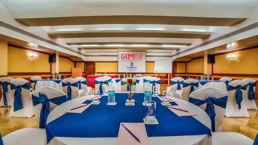 A formal banquet hall with blue tablecloths and a podium set for a corporate event. - Tara, Comfort Hotel in Hyderabad - Ramoji Film City.