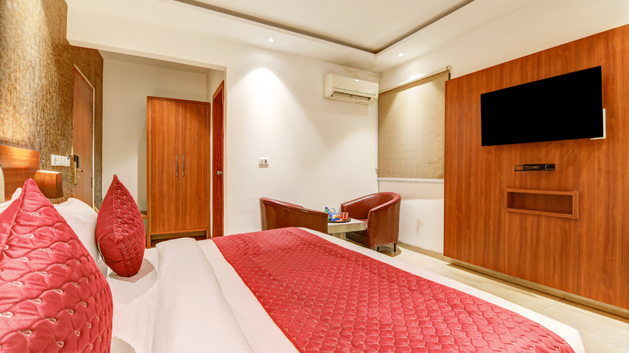 Wide-angle shot of the guest room featuring a wooden wardrobe, TV unit, and seating area - Hotel Velocity