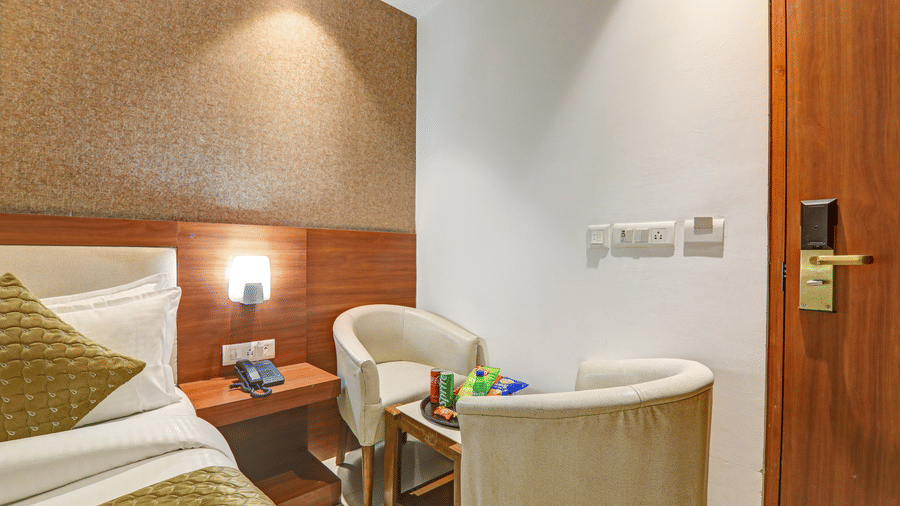 Bedside view of a gold-themed room showing a comfortable armchair and wooden nightstand - Hotel Velocity