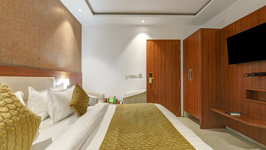 Side view of a premium room with gold bed runner, wooden wardrobe, and wall-mounted TV - Hotel Velocity