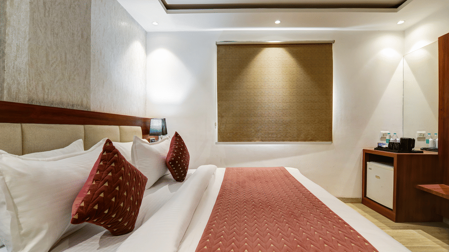 Side profile of a hotel bed with red pillows, matching runner, and a wood-panelled desk - Hotel Velocity