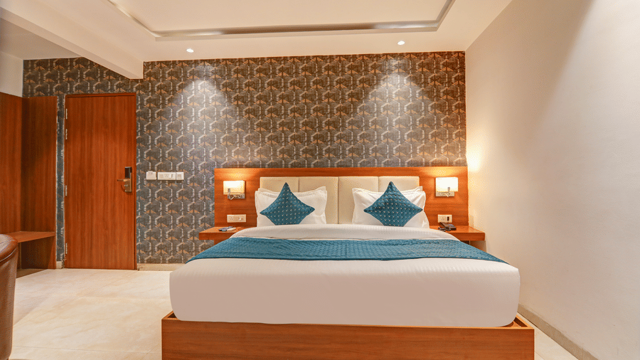 Front view of a king size bed with white linens, blue pillows, and patterned wallpaper - Hotel Velocity