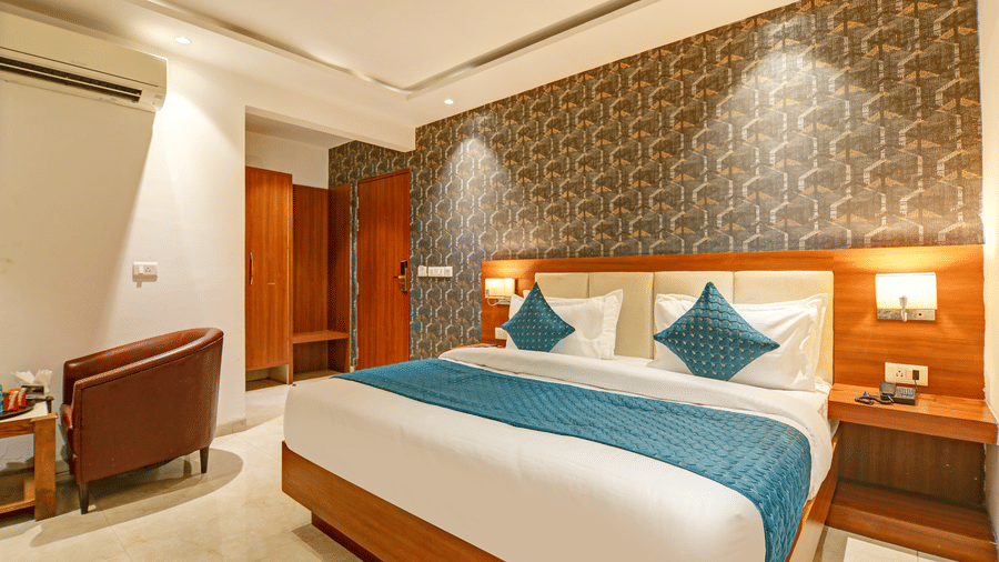 Elegant double bed with teal pillows, wood headboard, and decorative grey wallpaper - Hotel Velocity