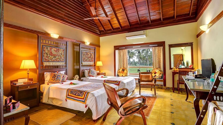 An image of a bedroom with seating area, open windows, lamp, dressing table, etc. -  Hoysala Village Resort, Hassan