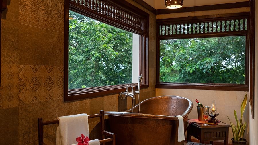 image of a copper bathtub with large glass windows at side at malnad attic suite -hoysala village resort, hassan