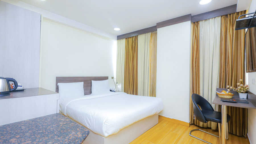 A bright hotel room featuring a bed, a desk, and large windows with privacy curtains - Hyphen Business Hotel, Noida
