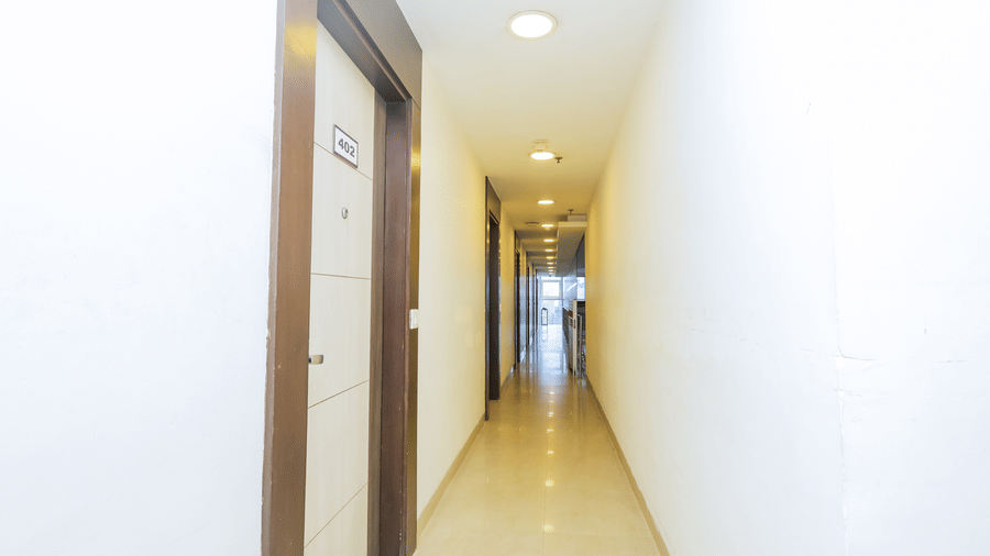 A simple and clean hotel corridor with white walls and dark wooden doors - Hyphen Business Hotel, Noida