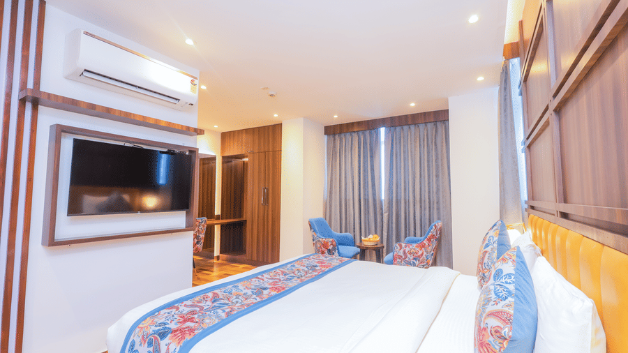 A bright hotel room featuring a comfortable bed, wall mounted television, and a blue armchair - Hyphen Business Hotel, Noida