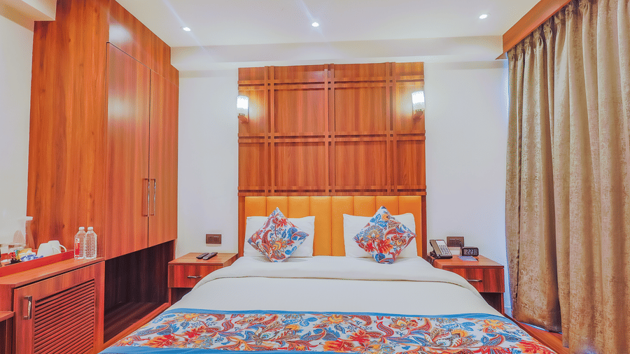 A well-decorated hotel room with a large bed, wooden furniture, and patterned bed linens - Hyphen Business Hotel, Noida