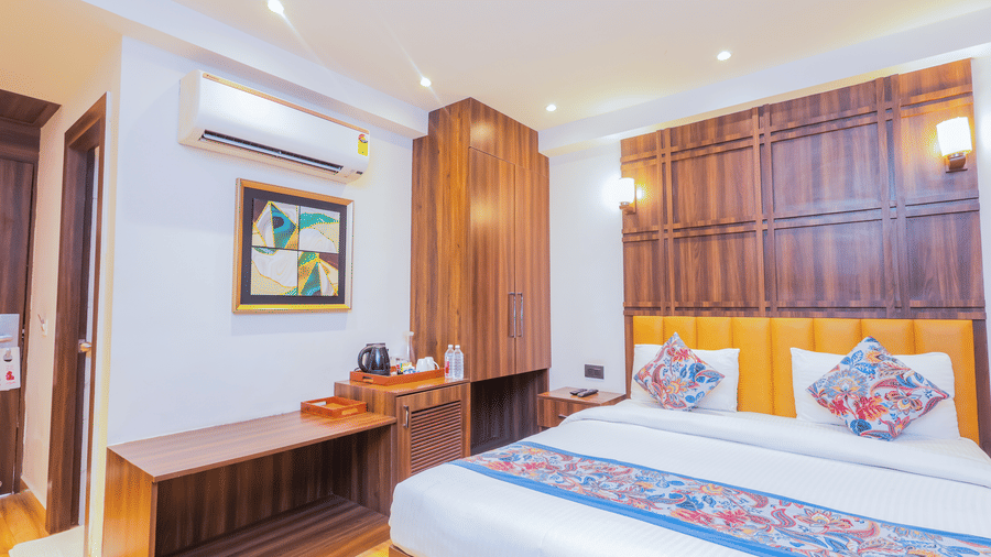 A neatly decorated hotel room with a large bed, wooden headboard, and a colourful bed runner - Hyphen Business Hotel, Noida