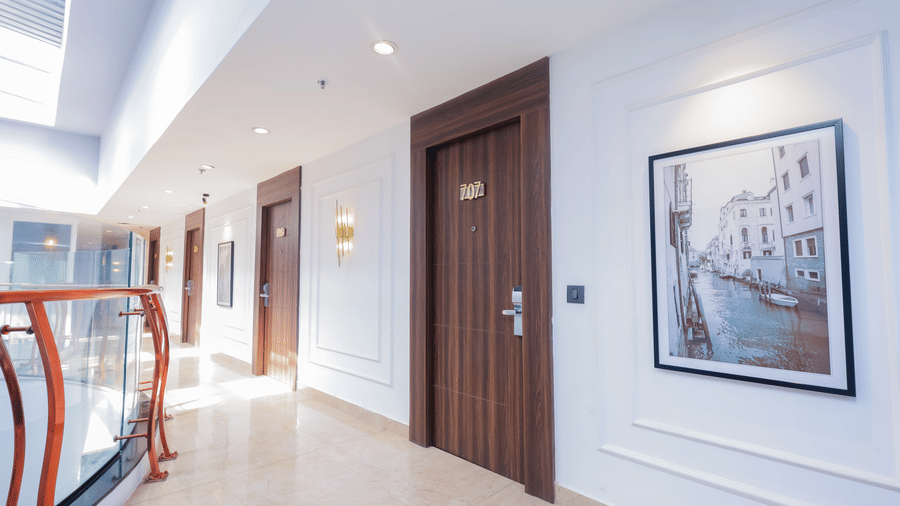 A brightly lit hotel corridor with white walls, wooden doors, and framed artwork - Hyphen Business Hotel, Noida