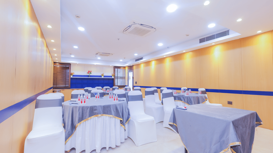 A conference room with tables arranged for a meeting or social gathering, featuring blue and white linens - Hyphen Business Hotel, Noida