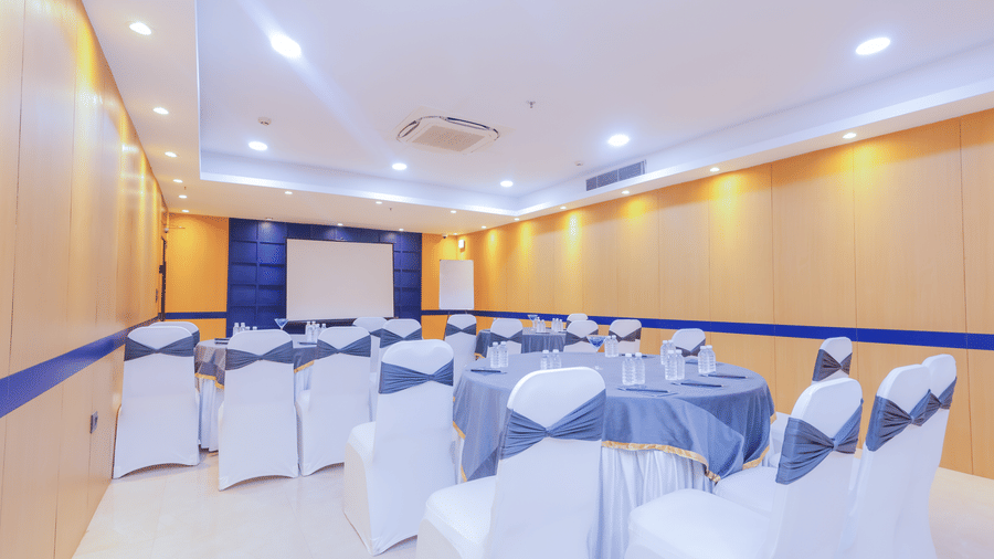 A conference room set up with round tables draped in blue and chairs with white covers - Hyphen Business Hotel, Noida