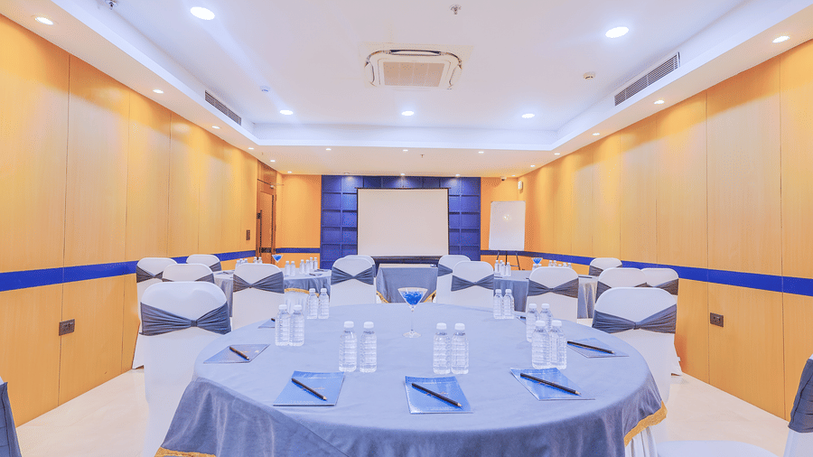 View of a spacious conference room with round tables and blue tablecloths, ready for an event - Hyphen Business Hotel, Noida