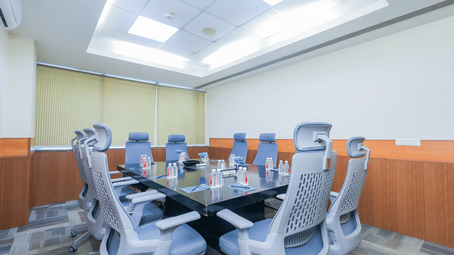 A modern conference room with a large boardroom table and ergonomic chairs set up for a meeting - Hyphen Business Hotel, Noida