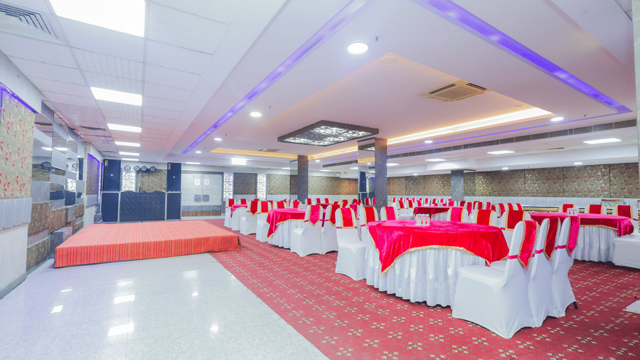 A banquet hall with red carpet, tables draped in red and white, and an elevated stage area - Hyphen Business Hotel, Noida
