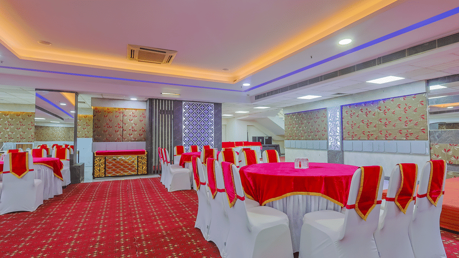 A large event space set up with round tables draped in red and white cloths, ready for a banquet - Hyphen Business Hotel, Noida