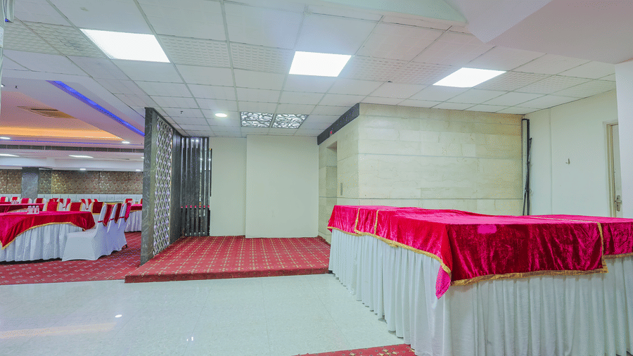 A wide view of a modern banquet hall featuring tables with red and white linens and a spacious layout - Hyphen Business Hotel, Noida