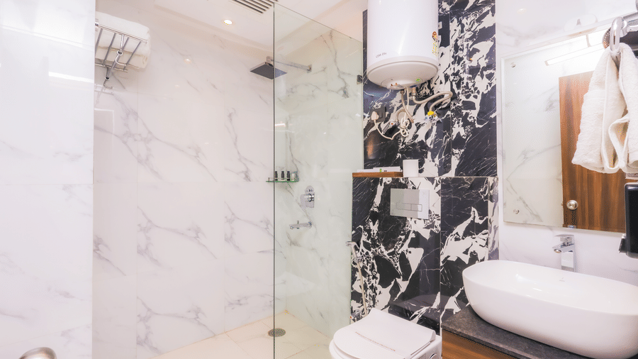A modern hotel bathroom featuring a glass shower enclosure, white sink, and black and white patterned tiles - Hyphen Business Hotel, Noida