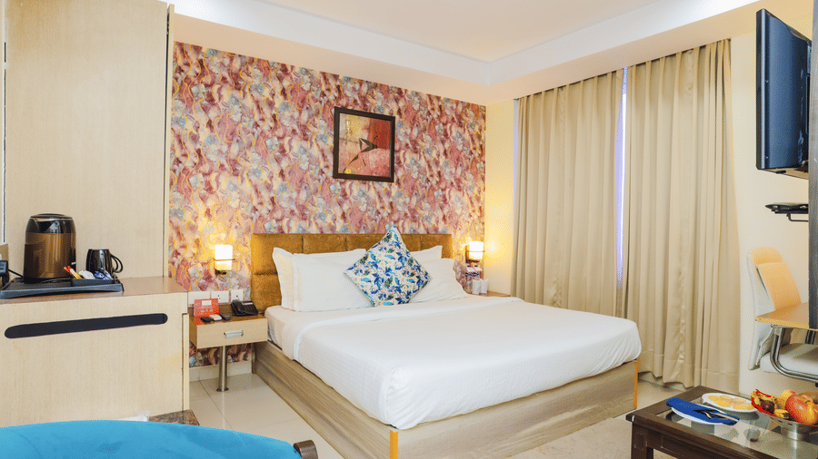 View of a hotel room with a single bed, patterned wallpaper, and a blue sofa - Hyphen Grand, Haridwar