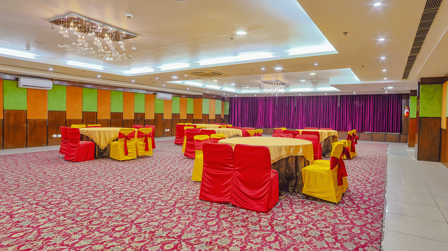 A banquet hall with tables draped in red and yellow cloths on a red patterned carpet - Hyphen Grand, Haridwar