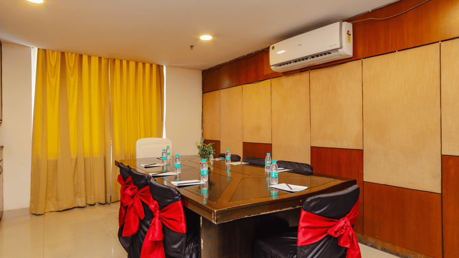 A compact boardroom set up with a dark table and red and black chairs - Hyphen Grand, Haridwar
