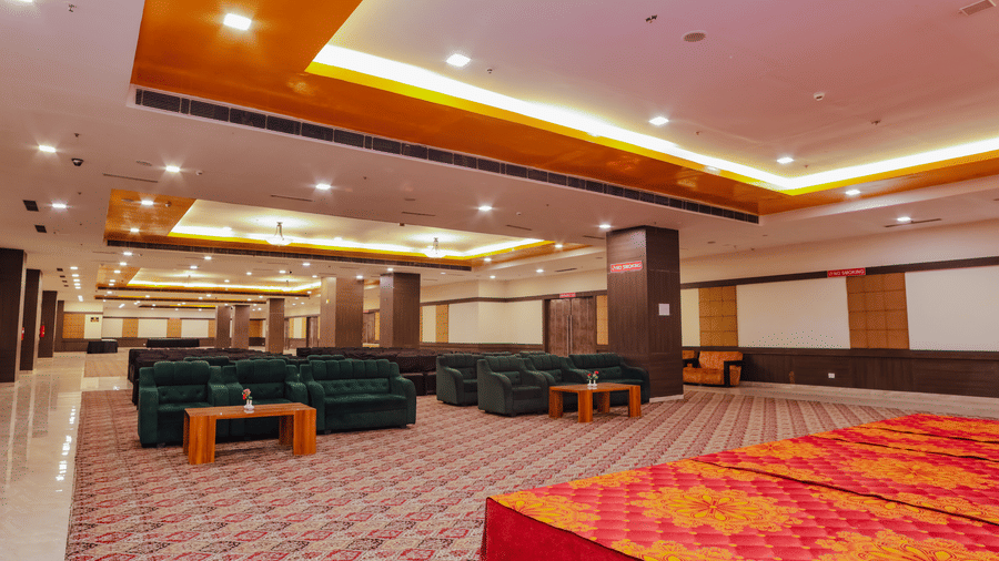 A spacious banquet hall area with red patterned carpet and a few sofas - Hyphen Grand, Haridwar