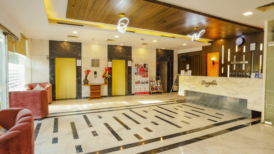 A long, well lit hotel corridor with wooden doors and framed pictures - Hyphen Grand, Haridwar