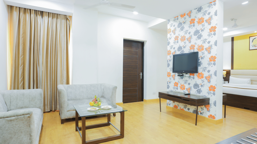 Suite living area at Hyphen Premier Hotel, Meerut, featuring a sofa, coffee table, and a decorative accent wall with a floral pattern.