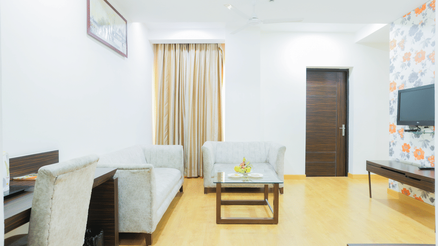 Wide view of a hotel suite's seating area at Hyphen Premier Hotel, Meerut, showing a sofa and a mounted television.