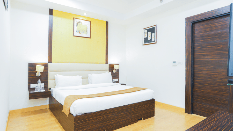 Spacious guest room at Hyphen Premier Hotel, Meerut, featuring a double bed, dark wood furniture, and minimalist design.