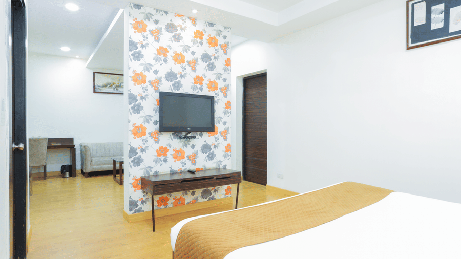 Spacious room at Hyphen Premier Hotel, Meerut, with a bed and an armchair featuring a distinctive white and grey floral print.