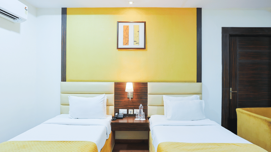 Twin beds in a guest room at Hyphen Premier Hotel, Meerut, with crisp white linens and a bold yellow accent panel above the beds.