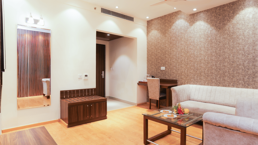 Well-lit suite featuring a cosy sofa set, wall-mounted mirror, and contemporary interiors at Hyphen Premier Hotel, Meerut.