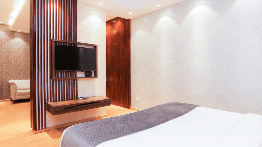 Spacious bedroom with partitioned TV wall, bed, and wall-mounted TV at Hyphen Premier Hotel, Meerut.