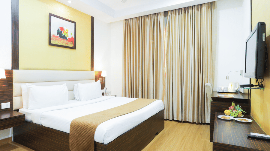 Well-furnished double bed room with elegant lighting, wooden flooring, and wall-mounted TV at Hyphen Premier Hotel, Meerut.