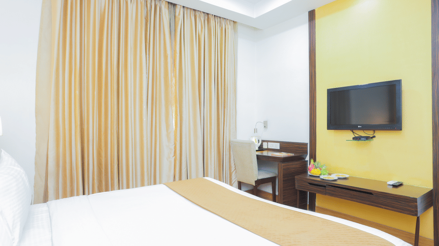 Bright and cosy guest room with a large bed, flat-screen TV, and floor-to-ceiling curtains at Hyphen Premier Hotel, Meerut.