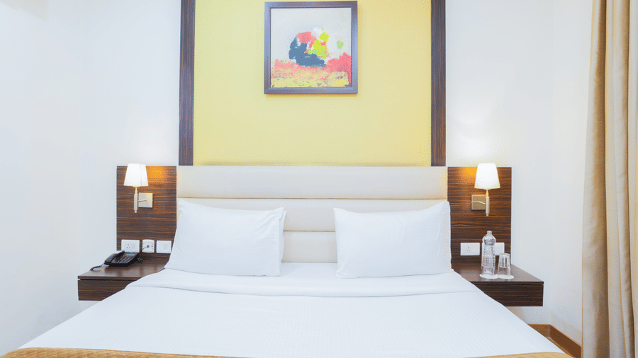 A room featuring a comfortable double bed, bedside table, and simple decor at Hyphen Premier Hotel, Meerut.