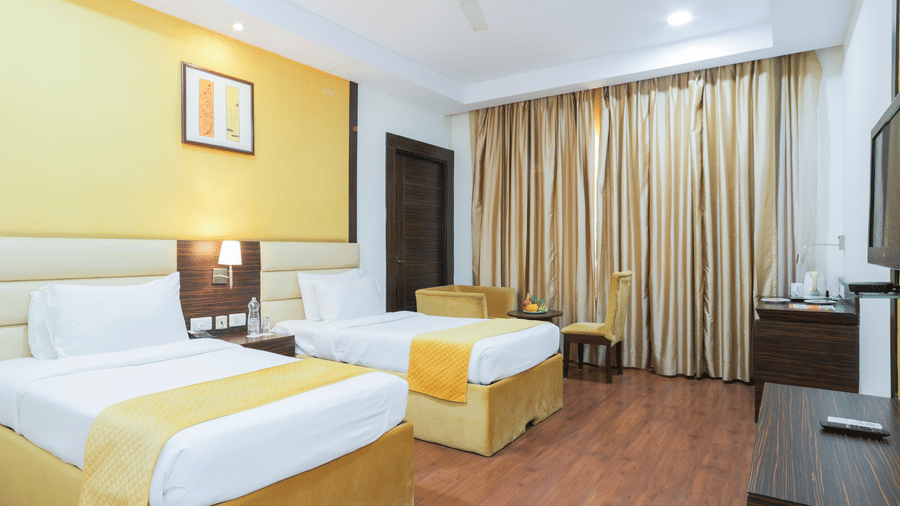 Spacious twin-bed room with wooden flooring, work desk, and ceiling-to-floor curtains at Hyphen Premier Hotel, Meerut.