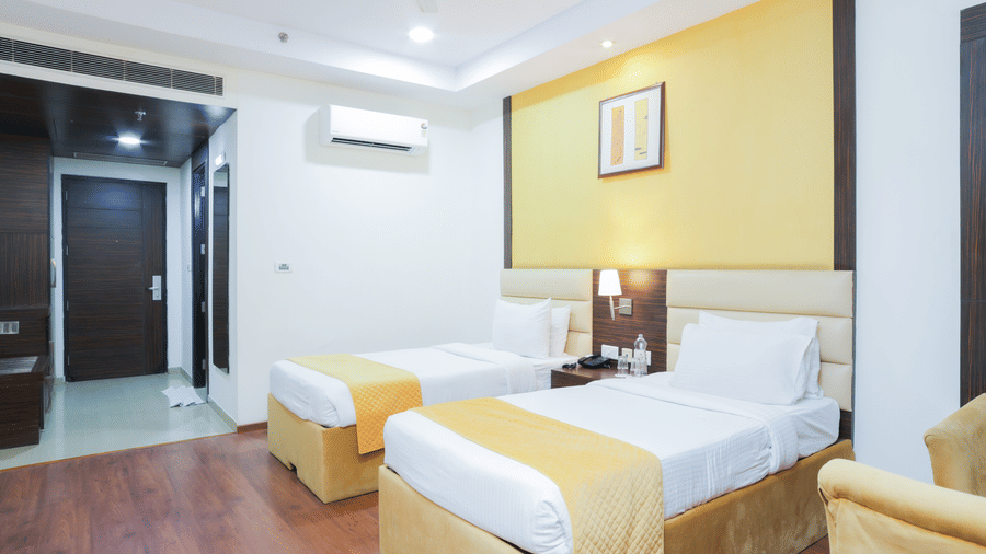 Twin-bed guest room with warm lighting, wooden flooring, and minimalistic design at Hyphen Premier Hotel, Meerut.