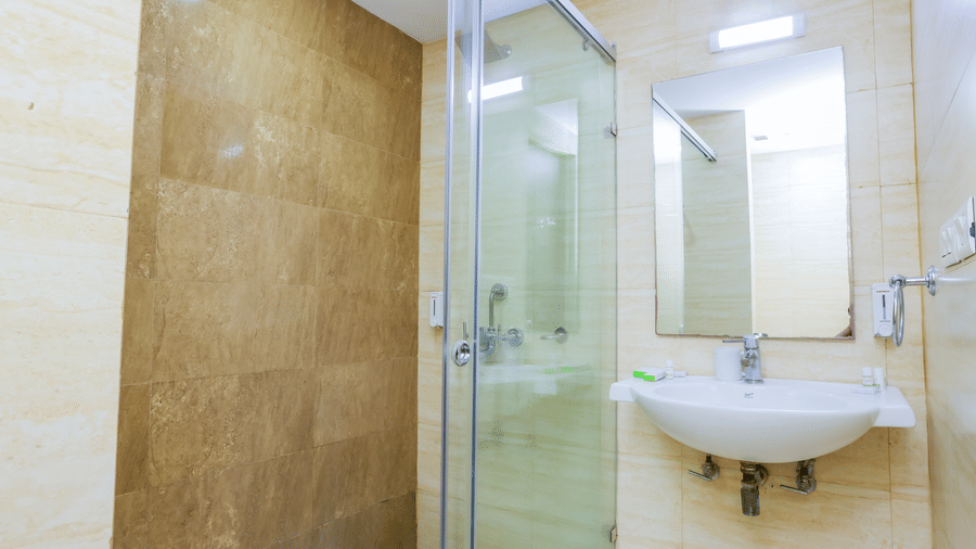 Modern bathroom with glass shower enclosure and beige-toned wall tiles at Hyphen Premier Hotel, Meerut.