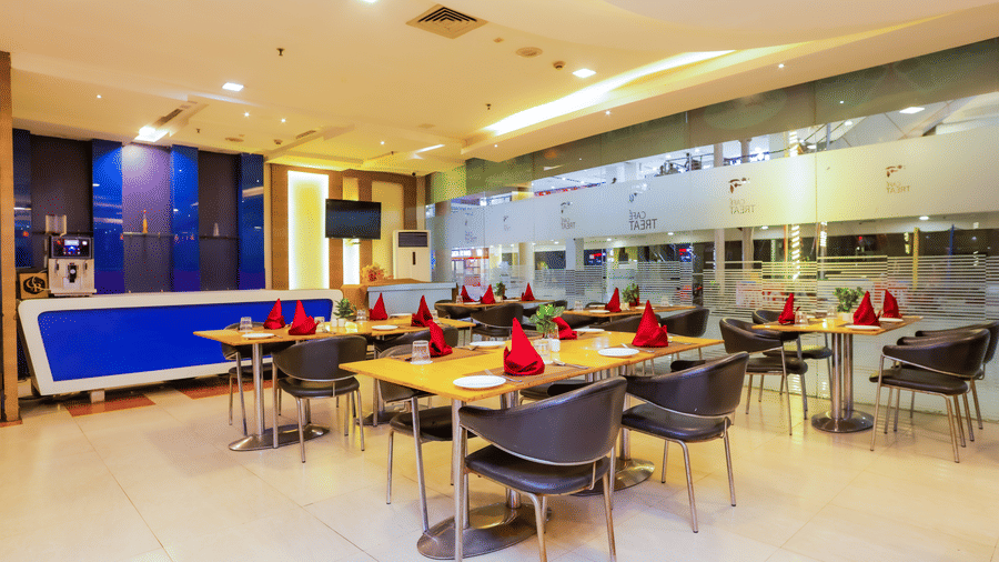 Dining area with glass partition and modern seating at Cafe Treat - Hyphen Premier Hotel, Meerut.