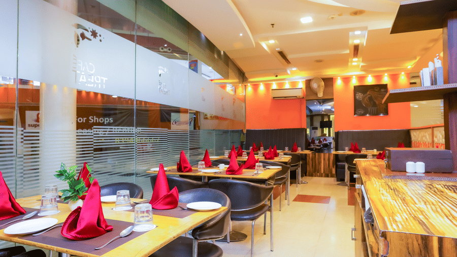 Bright restaurant interior with red napkin setups and wooden accents at Cafe Treat - Hyphen Premier Hotel, Meerut.