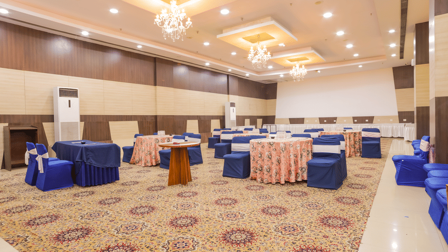 Brightly lit conference hall with chandelier lighting and cluster seating arrangement at Hyphen Premier Hotel, Meerut.